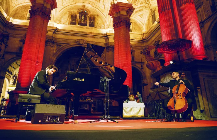 Dos personas: una tocando el piano y otra el chelo, en una iglesia