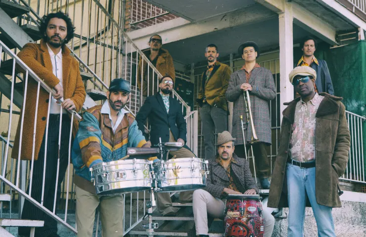 componentes del grupo en unas escaleras, algunos sentados con instrumentos de percusión y otros de pie