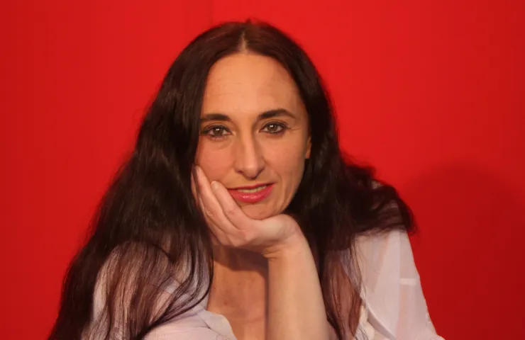 mujer con pelo largo, cara de felicidad, apoya su cara sobre la palma de una mano, fondo rojo
