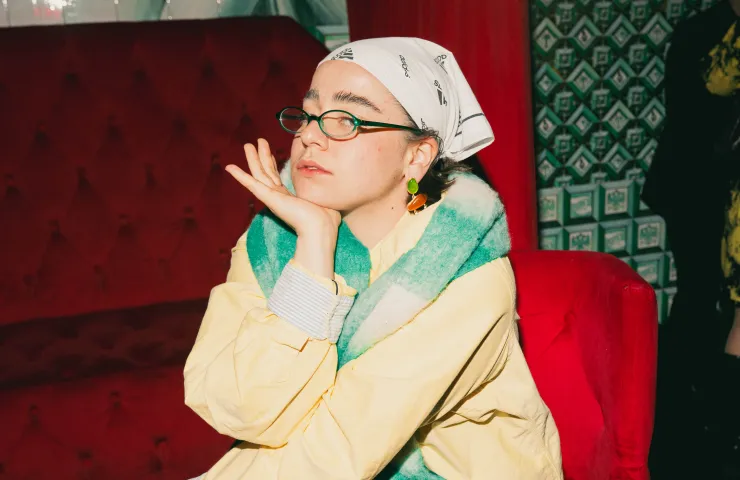 chica sentada con pañuelo en la cabeza, gafas, apoya su cabeza en la mano