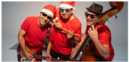 tres hombres con camisetas rojas de manga corta, gorro de papa Noel rojo y blanco, gafas de sol negras, cada uno con un instrumento musical en las manos